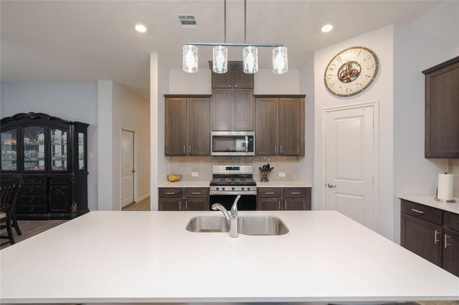 Kitchen featuring sink, stainless steel appliances, backsplash, an island with sink, and dark brown cabinets