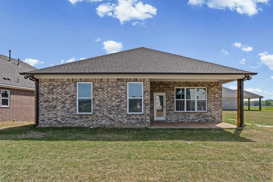 Back of property featuring brick siding, a patio area, a yard, and roof with shingles