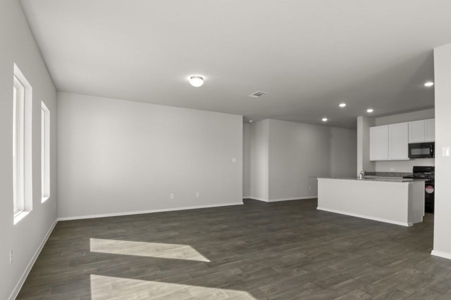 Image of a living room with light grey walls, dark brown flooring, a center island in the distance and windows