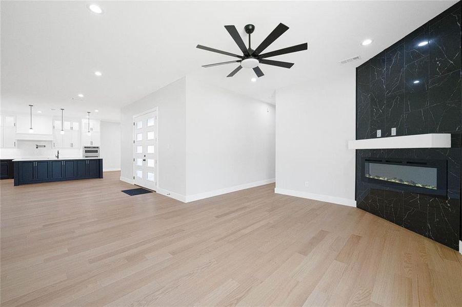 Unfurnished living room featuring light wood-type flooring, ceiling fan, recessed lighting, a large fireplace, and baseboards Unfurnished living room featuring light wood-type flooring, ceiling fan, recessed lighting, a large fireplace, and baseboards