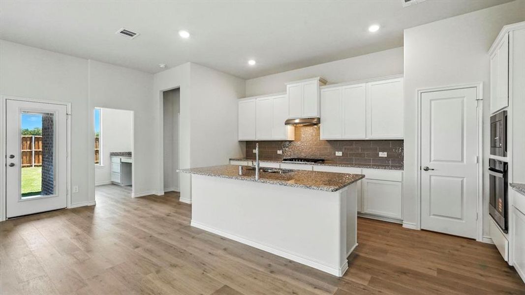Modern kitchen featuring a central island with a sink, white cabinetry, integrated stainless steel appliances, and wood-finish flooring Modern kitchen featuring a central island with a sink, white cabinetry, integrated stainless steel appliances, and wood-finish flooring