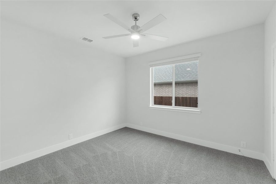 Empty bedroom with gray carpet, white walls, ceiling fan, and single window