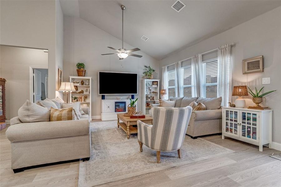 Living room featuring high vaulted ceiling, a ceiling fan, light wood-style floors, and a glass covered fireplace Living room featuring high vaulted ceiling, a ceiling fan, light wood-style floors, and a glass covered fireplace