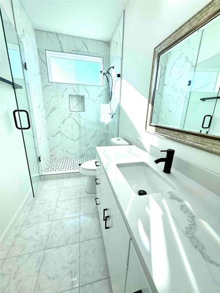 Full bath featuring vanity, light marble finish floors, and a marble finish shower