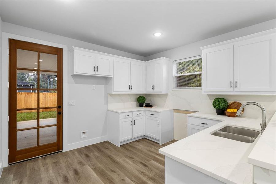 Kitchen featuring white cabinets, sink, light stone countertops, light wood-type flooring, and tasteful backsplash