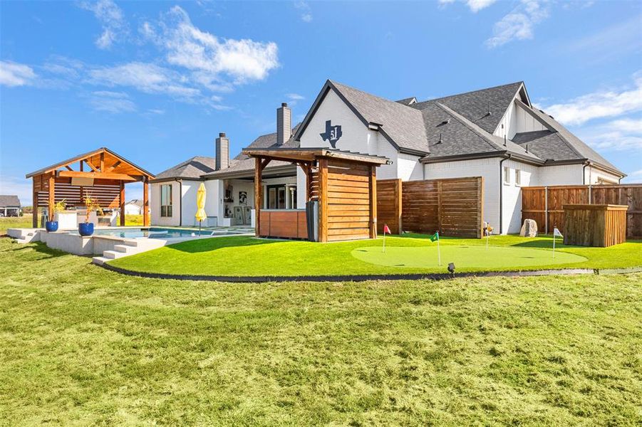 Rear view of house with a putting green, a swimming pool, hot tub, and a patio area.