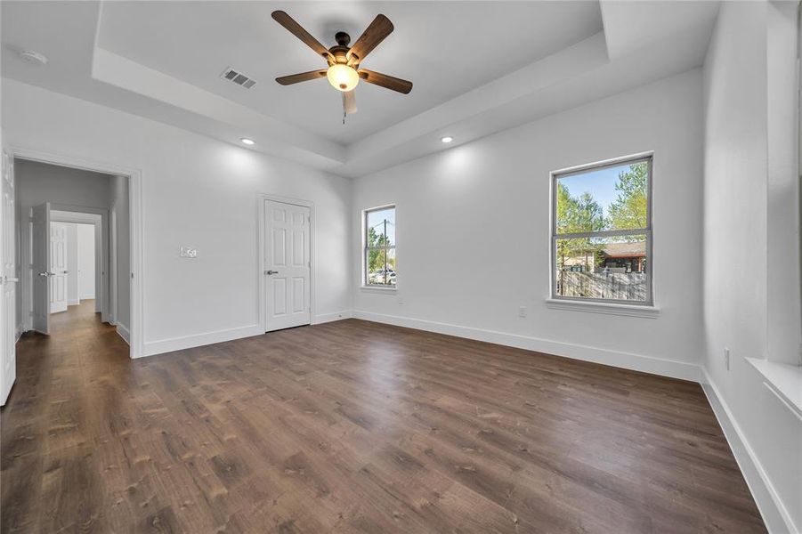 Unfurnished bedroom featuring a tray ceiling, dark wood-type flooring, baseboards, and visible vents