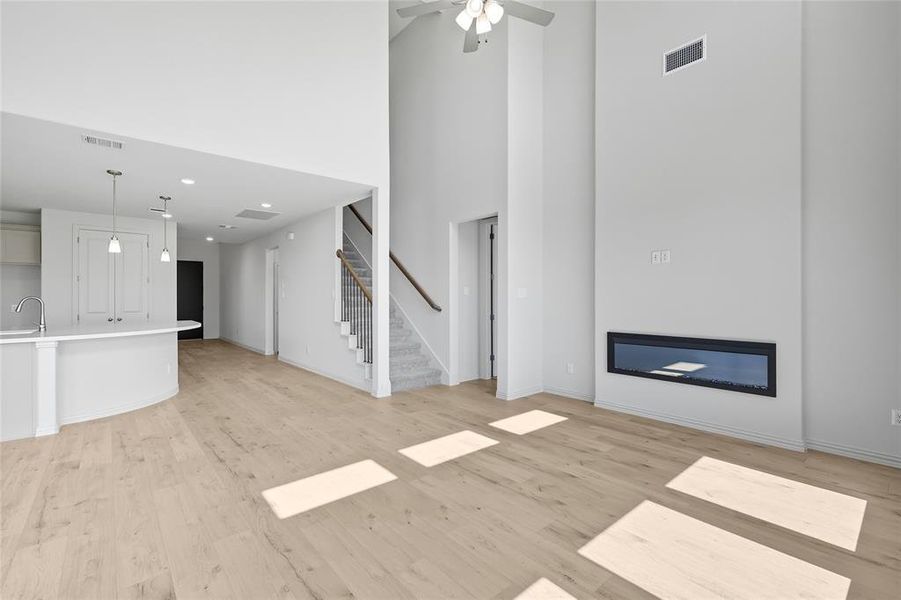Unfurnished living room featuring a towering ceiling, light wood-type flooring, a ceiling fan, and stairs Unfurnished living room featuring a towering ceiling, light wood-type flooring, a ceiling fan, and stairs