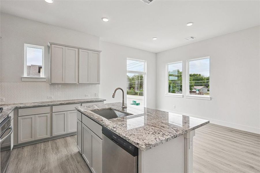 Kitchen featuring tasteful backsplash, stainless steel appliances, a center island with sink, sink, and light wood-type flooring