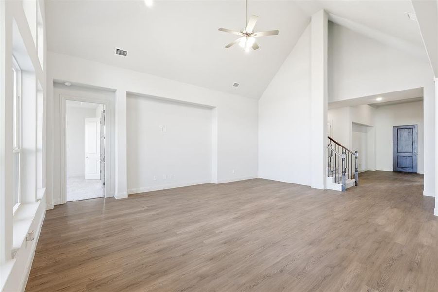 Unfurnished living room with high vaulted ceiling, stairs, light wood finished floors, ceiling fan, and recessed lighting Unfurnished living room with high vaulted ceiling, stairs, light wood finished floors, ceiling fan, and recessed lighting