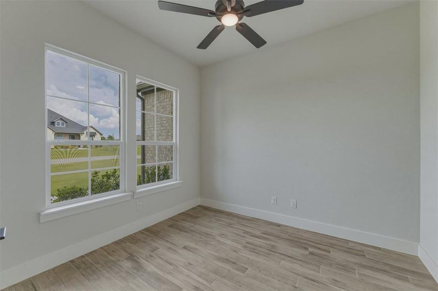 Light-filled room featuring two multi-pane windows, wood-finish flooring, a ceiling fan with integrated lighting, and neutral wall tones Light-filled room featuring two multi-pane windows, wood-finish flooring, a ceiling fan with integrated lighting, and neutral wall tones