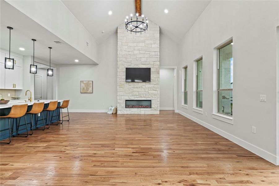 Living room with high vaulted ceiling, light wood-style flooring, a fireplace, a chandelier, and wet bar Living room with high vaulted ceiling, light wood-style flooring, a fireplace, a chandelier, and wet bar