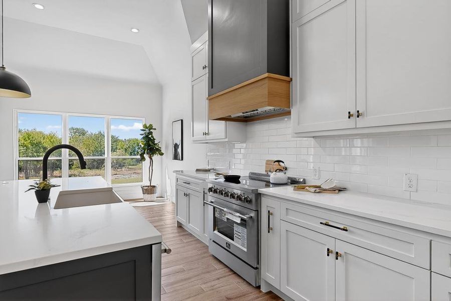 Kitchen with high end stainless steel range oven, light countertops, light wood-style floors, wall chimney exhaust hood, and recessed lighting