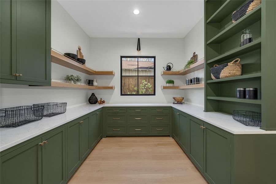 Spacious pantry featuring extensive green cabinetry with gold-toned hardware, light wood-finish flooring, and white countertops