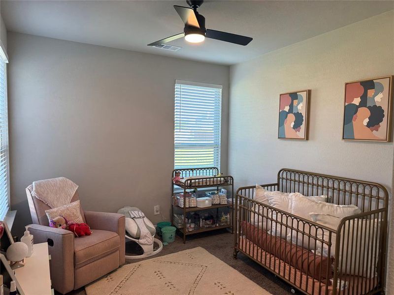 Carpeted bedroom featuring a ceiling fan and a nursery area Carpeted bedroom featuring a ceiling fan and a nursery area