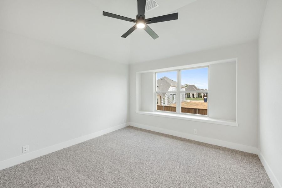 Empty bedroom with gray carpet, white walls, ceiling fan, and large window overlooking neighborhood homes.