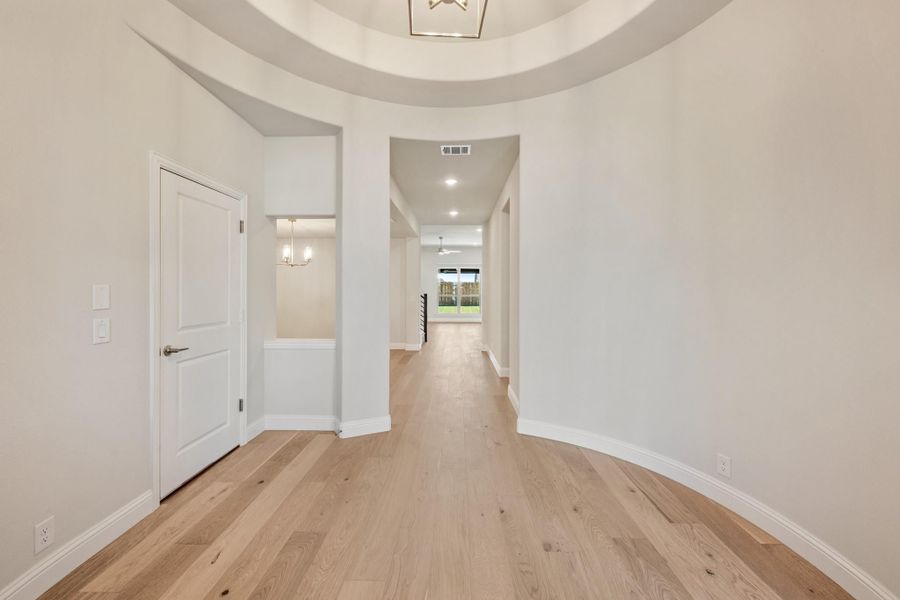 Curved entryway with round tray ceiling, pendant light, and light hardwood floors leading to hallway Curved entryway with round tray ceiling, pendant light, and light hardwood floors leading to hallway
