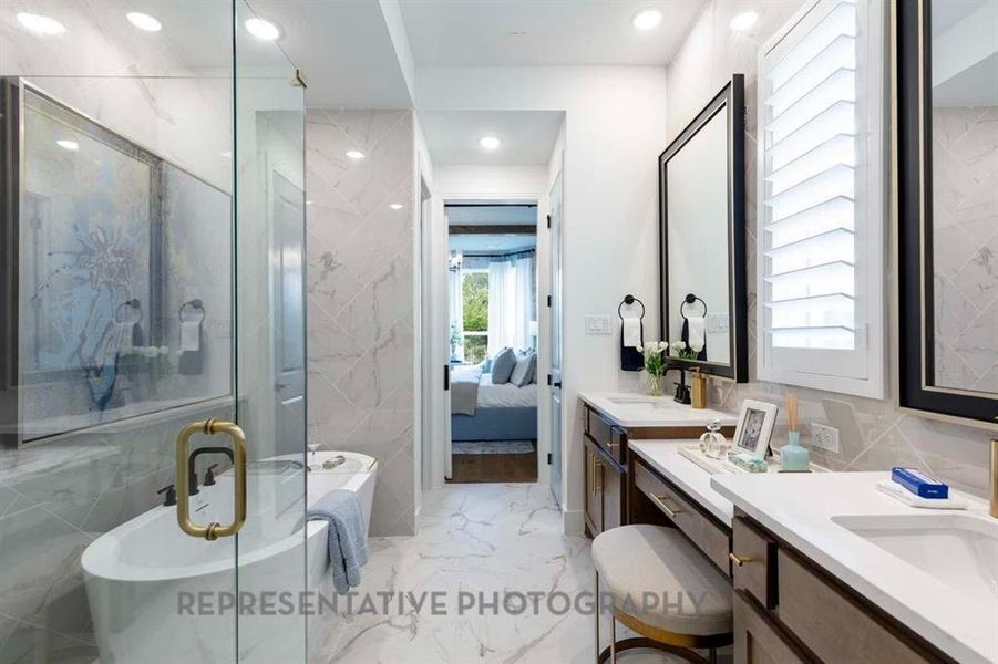 Ensuite bathroom featuring light marble finish flooring, a freestanding bath, tile walls, a stall shower, and vanity