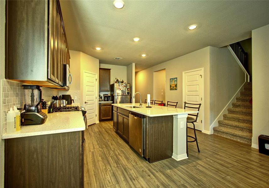Kitchen with a kitchen breakfast bar, stainless steel appliances, a center island with sink, light stone counters, and recessed lighting Kitchen with a kitchen breakfast bar, stainless steel appliances, a center island with sink, light stone counters, and recessed lighting