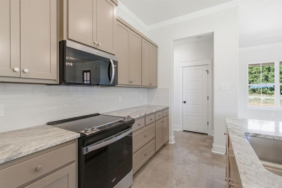 Kitchen featuring electric stove, finished concrete flooring, stainless steel microwave, gray cabinets, and decorative backsplash