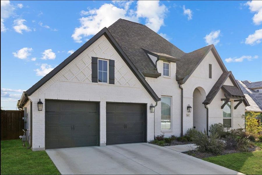French country inspired facade with brick siding, concrete driveway, and roof with shingles