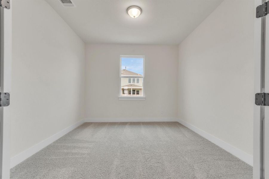 A well-lit, neutral-toned room featuring a single window and soft carpet underfoot.