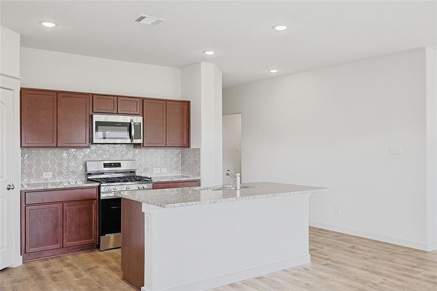 Kitchen featuring stainless steel appliances, light hardwood / wood-style flooring, a center island with sink, and sink