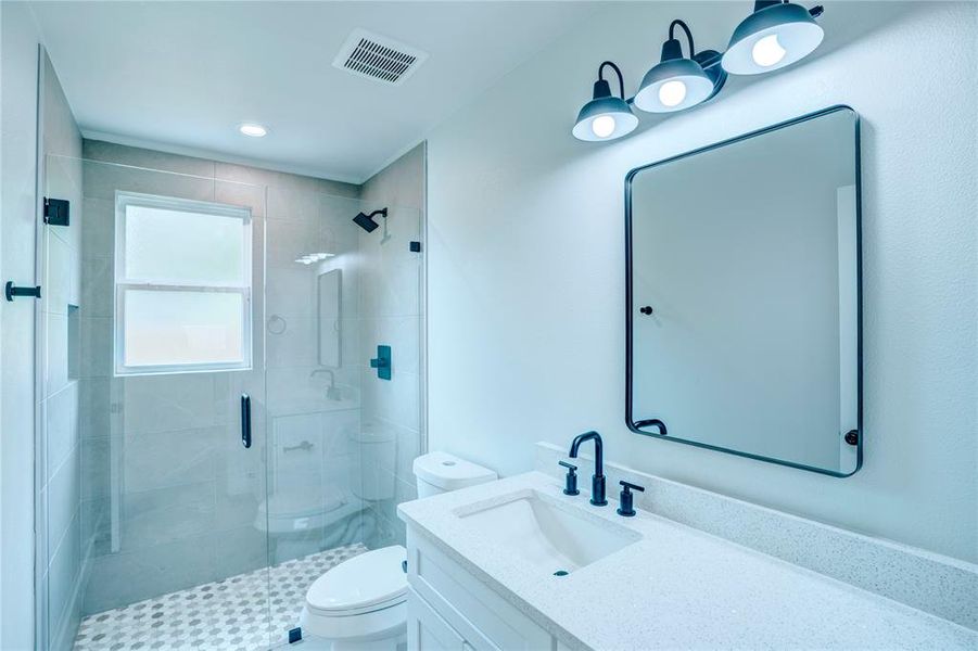 Modern bathroom featuring a frameless glass shower enclosure, a vanity with an integrated sink and light-colored countertop, matte black fixtures, a contemporary framed mirror, and a three-light vanity fixture