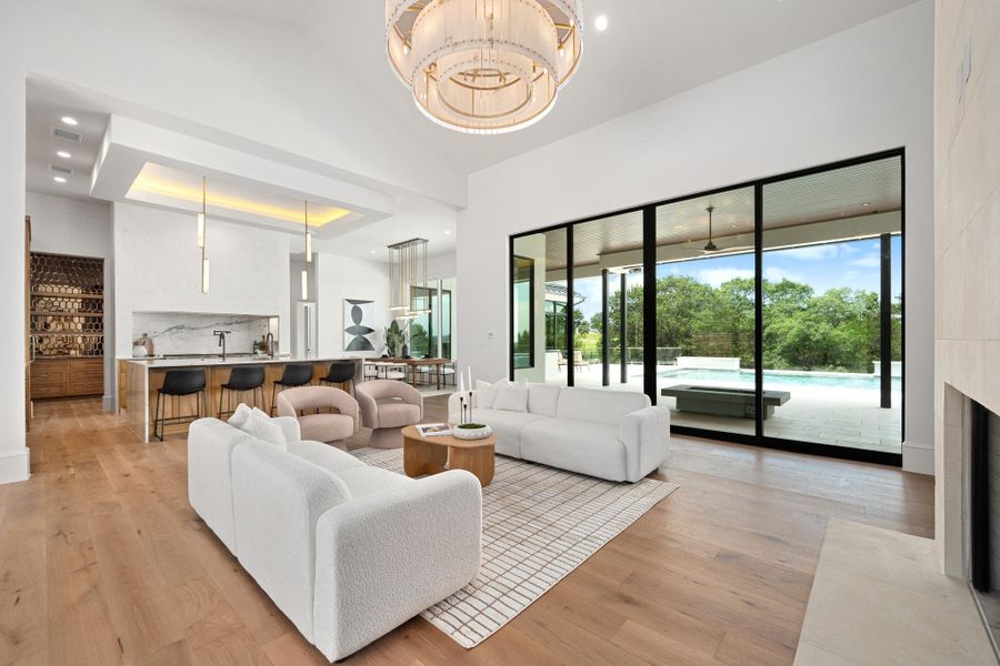 An open concept living area boasts a sleek fireplace, high ceilings, and expansive sliding glass doors leading to an outdoor oasis.