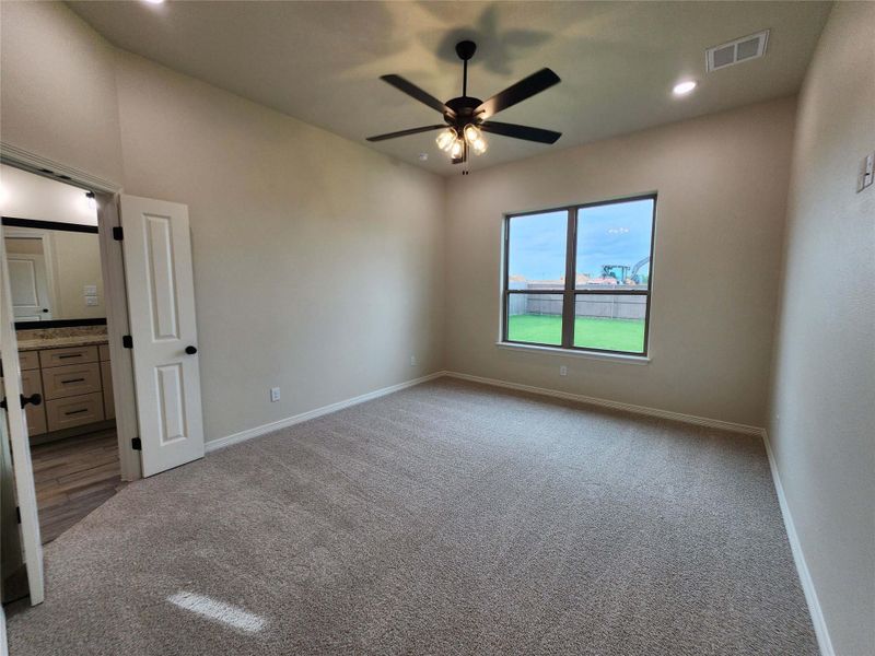 Spacious room featuring neutral carpeting, a large window overlooking a green lawn, and a ceiling fan with integrated lighting