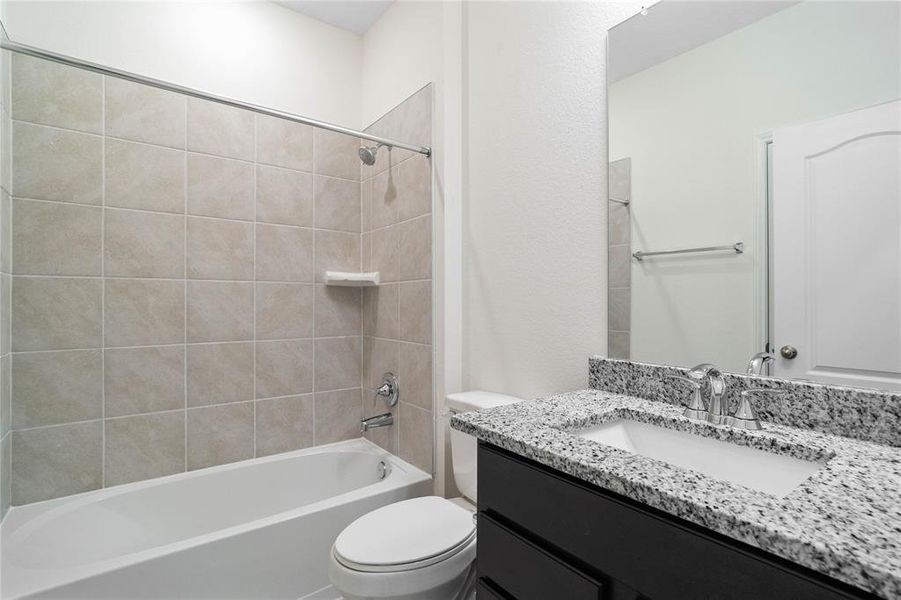 Secondary bathroom features granite countertops and stained cabinets, neutral paint, shower/tub combo with tile surround, large mirror, tile floors, and sleek fixtures and modern finishes.