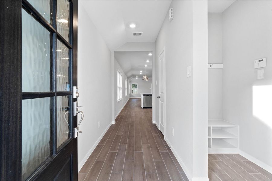 This entryway features a modern, open-concept design. The long, bright corridor utilizes a neutral color palette, recessed lighting, and floor tiles to lead the eye toward the home's main living area.