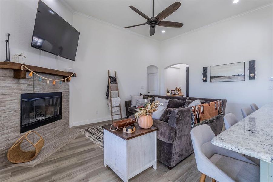 Living room with light hardwood / wood-style floors, ceiling fan, a tiled fireplace, and ornamental molding