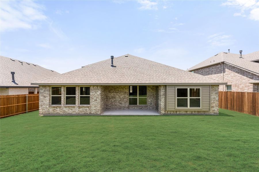 Rear view of single-story brick home with covered patio, large green backyard, and wood privacy fence. Rear view of single-story brick home with covered patio, large green backyard, and wood privacy fence.