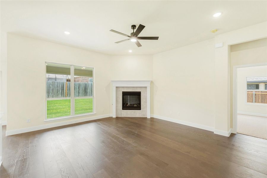Open living room with hardwood floors, tile fireplace, ceiling fan, and large backyard-facing window Open living room with hardwood floors, tile fireplace, ceiling fan, and large backyard-facing window