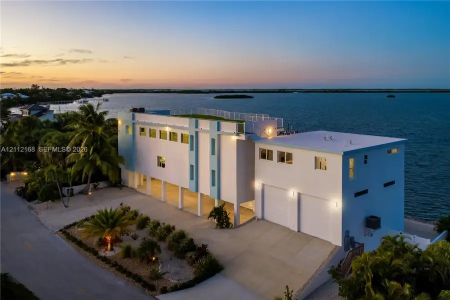 Waterfront residence featuring a rooftop terrace, multi-level exterior structure, two-car garage, concrete driveway, and pilings foundation Waterfront residence featuring a rooftop terrace, multi-level exterior structure, two-car garage, concrete driveway, and pilings foundation