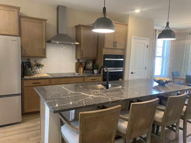 Kitchen with wall chimney range hood, tasteful backsplash, freestanding refrigerator, double oven, and dark stone counters