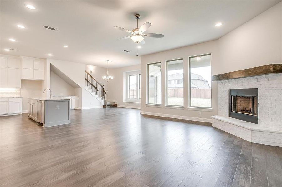 Unfurnished living room featuring sink, a brick fireplace, hardwood / wood-style flooring, and ceiling fan with notable chandelier