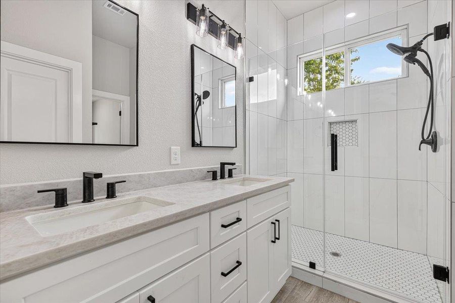 Dual vanities with stone counters and modern fixtures anchor this well-appointed bathroom, featuring a spacious glass-enclosed shower. Dual vanities with stone counters and modern fixtures anchor this well-appointed bathroom, featuring a spacious glass-enclosed shower.