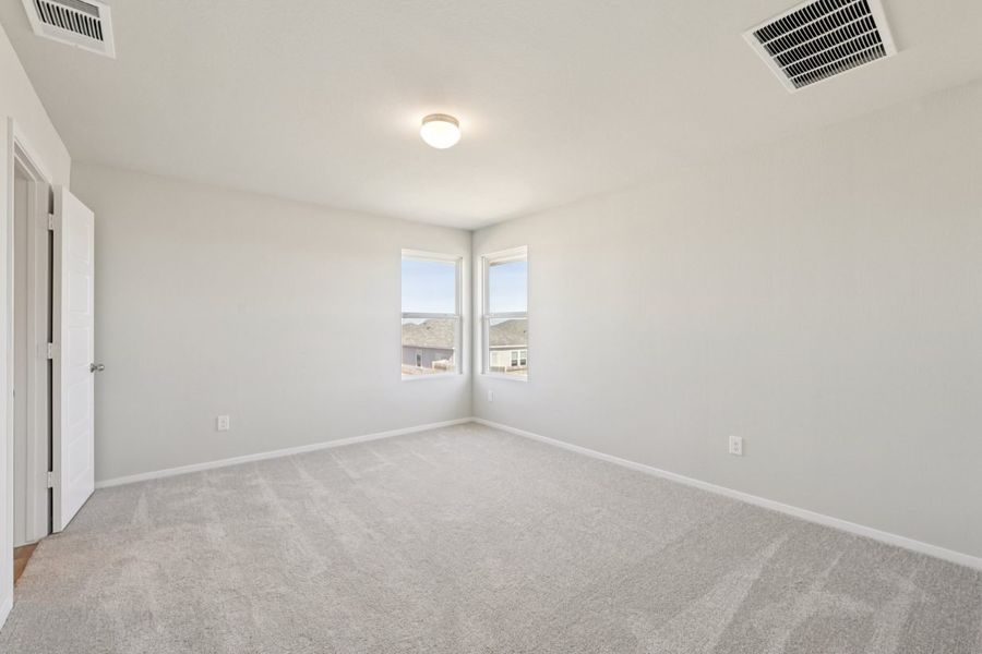 Image of a primary bedroom with tan carpeting, grey walls, windows and white trim
