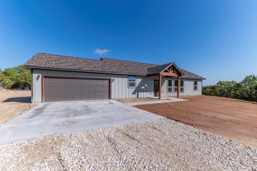 View of front facade with driveway, roof with shingles, an attached garage, and board and batten siding