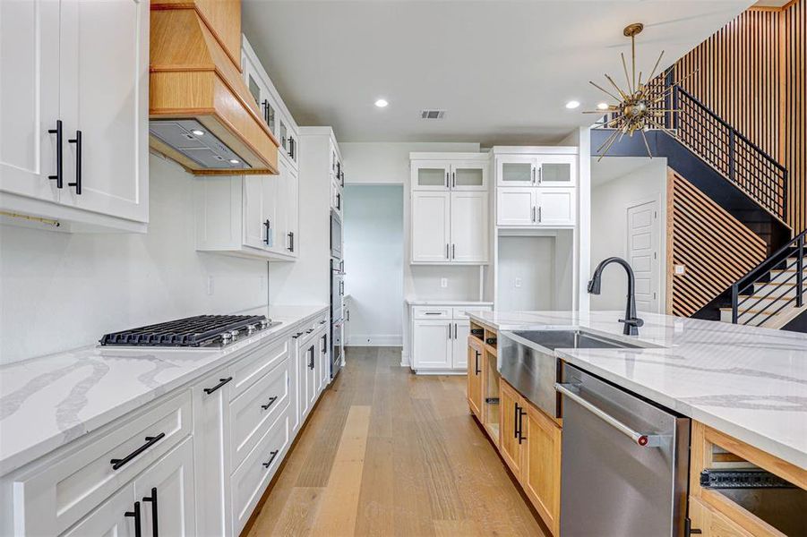 Kitchen featuring appliances with stainless steel finishes, premium range hood, light wood finished floors, glass insert cabinets, and recessed lighting