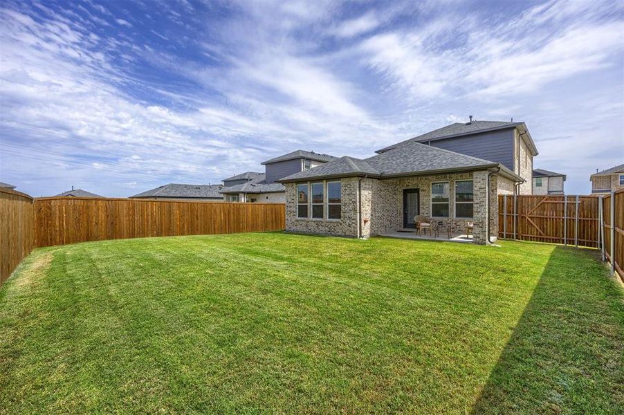 Expansive backyard featuring a lush lawn, privacy fencing, and a covered patio