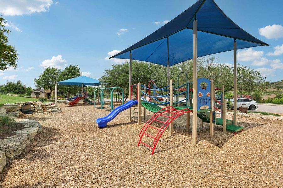 Community playground featuring multiple play structures with slides, climbing elements, and shade covers