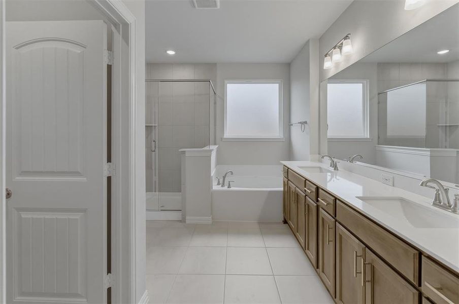 Bathroom featuring a dual vanity with undermount sinks, a large mirror, a separate soaking tub, a glass-enclosed shower, and tile flooring