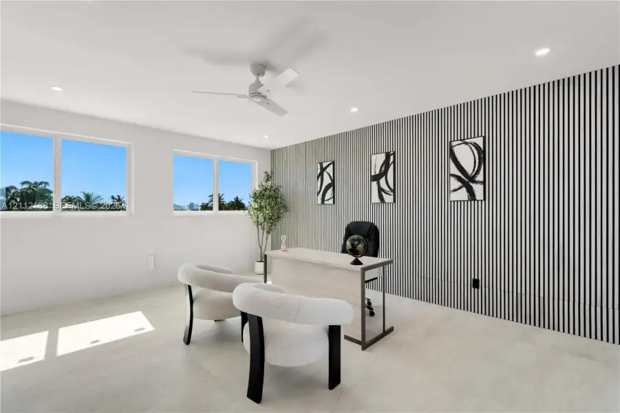 Room featuring large windows, neutral stone-finish flooring, recessed lighting, a modern ceiling fan, and a decorative vertical-slat accent wall Room featuring large windows, neutral stone-finish flooring, recessed lighting, a modern ceiling fan, and a decorative vertical-slat accent wall