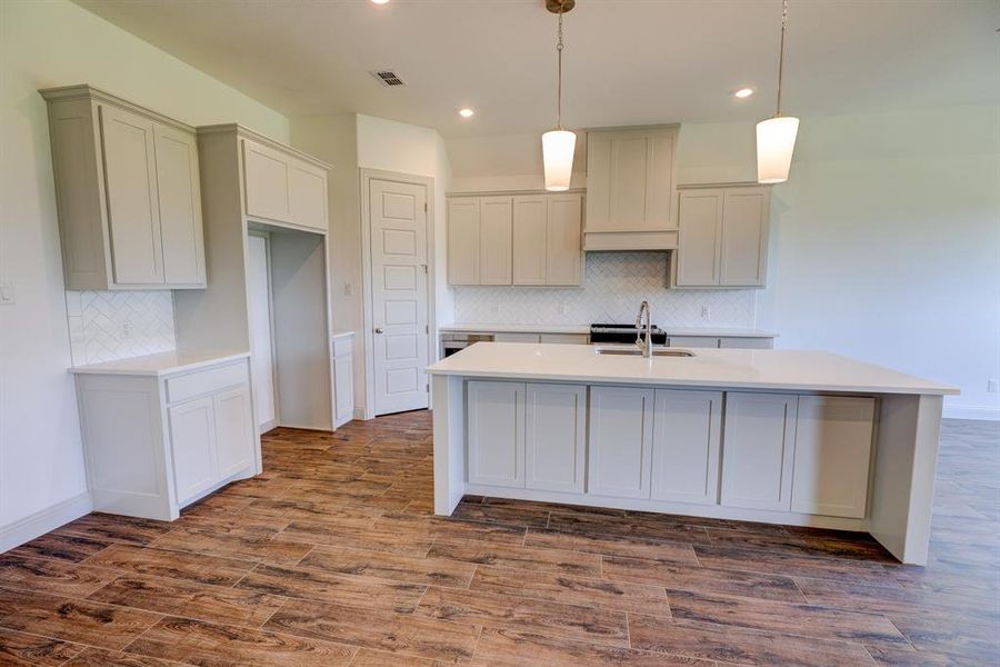 Kitchen featuring backsplash, light stone countertops, pendant lighting, an island with sink, and dark wood-style floors Kitchen featuring backsplash, light stone countertops, pendant lighting, an island with sink, and dark wood-style floors