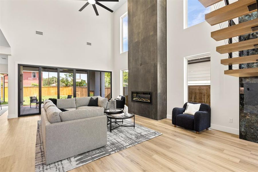 Vaulted living space featuring a floor-to-ceiling fireplace with an inset electric firebox, an open-tread staircase with wood risers, a ceiling fan, and wood-finish flooring