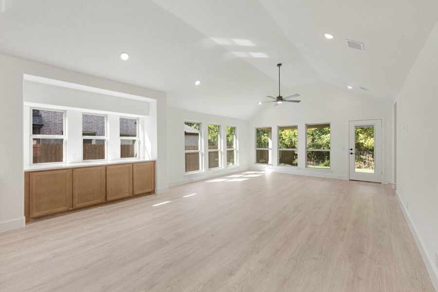 Bright open living room with vaulted ceiling, light wood floors, ceiling fan, and large windows with backyard views.