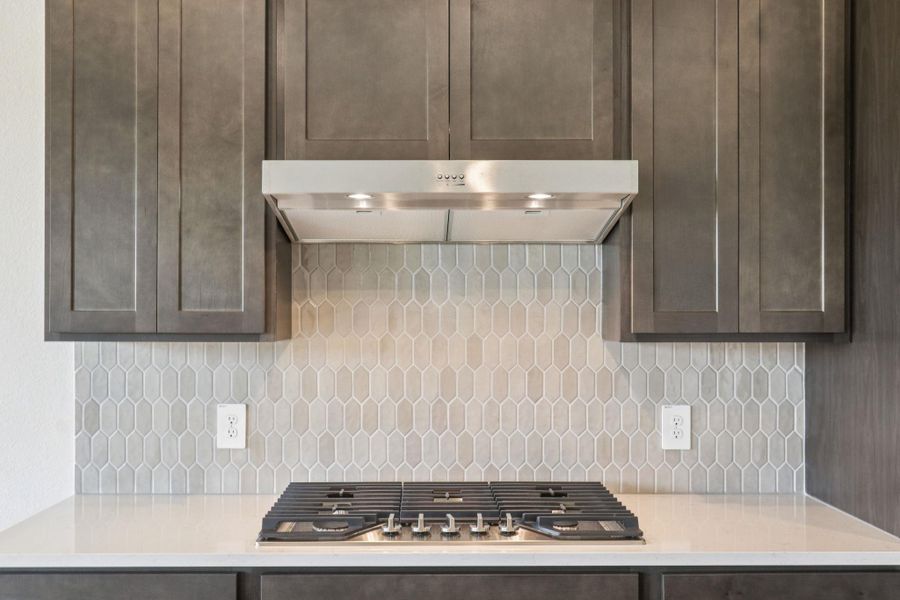 Kitchen with dark brown cabinetry, under cabinet range hood, light stone counters, and decorative backsplash Kitchen with dark brown cabinetry, under cabinet range hood, light stone counters, and decorative backsplash